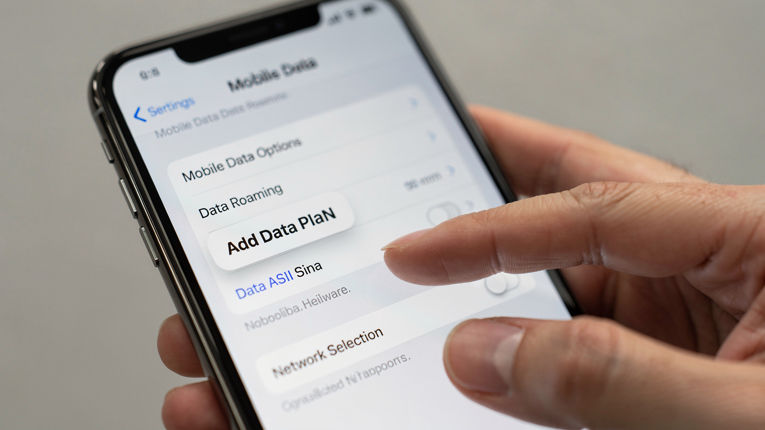 Primer plano de un iPhone actual mostrando la pantalla de configuración de datos móviles con la opción de 'Añadir plan de datos' visible, con los dedos de una persona tocando la pantalla.