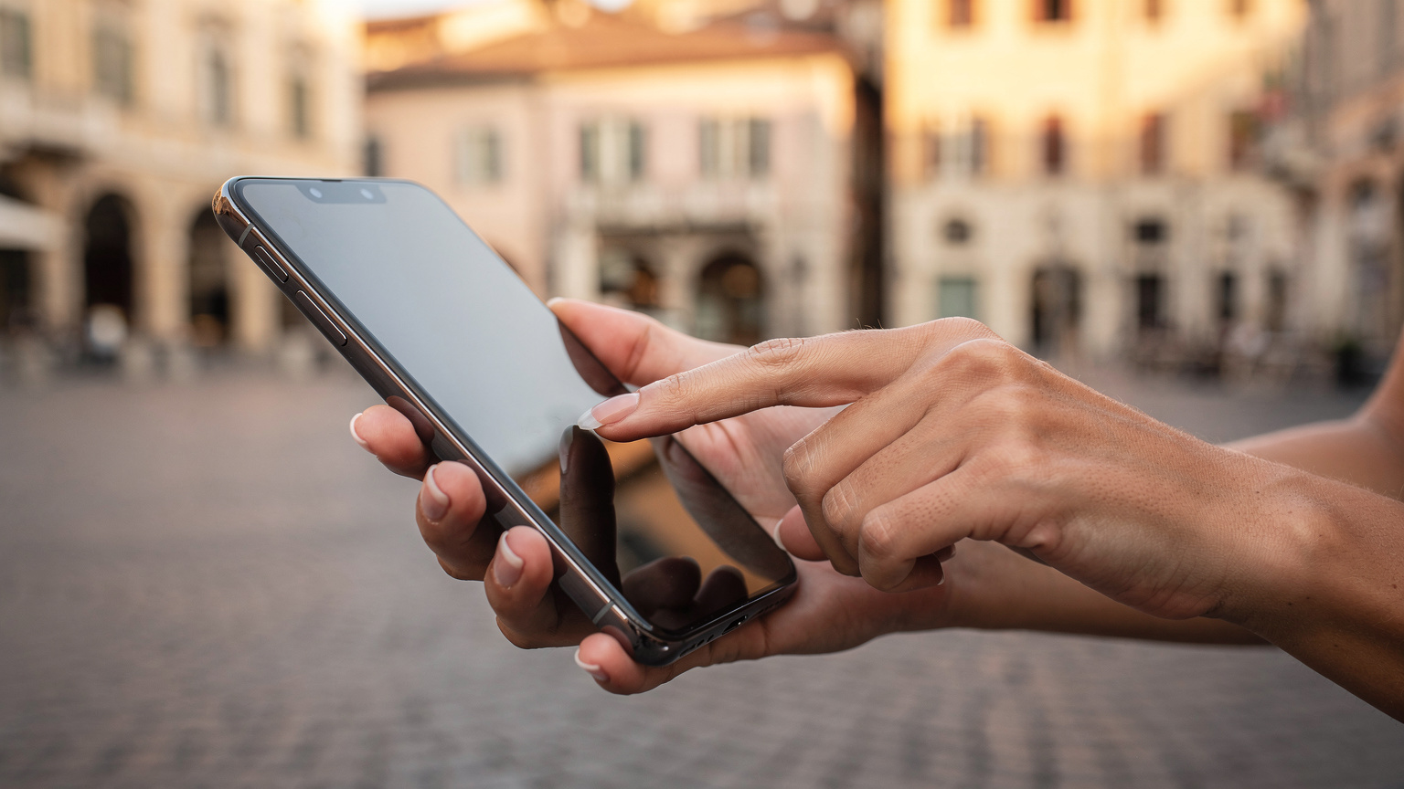 A close-up of a hand gently tapping a smartphone screen, indicating the seamless activation of an eSIM for European travel, against a blurred background of a charming Italian piazza.