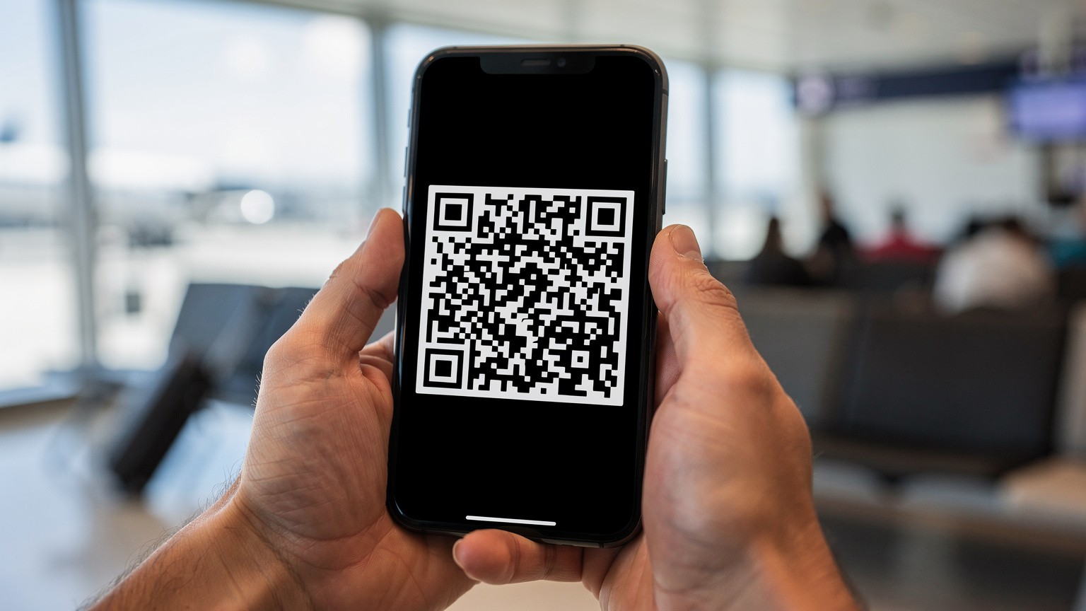 Nahaufnahme von Händen, die ein Smartphone halten, auf dem ein QR-Code zur eSIM-Installation angezeigt wird. Im Hintergrund ist eine unscharfe Flughafen-Lounge zu sehen.