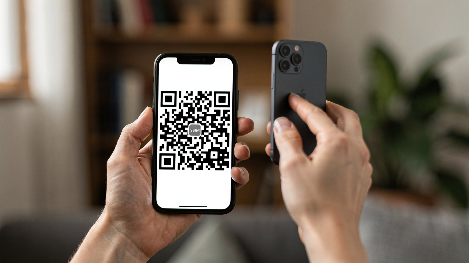 Крупный план женских рук, держащих смартфон, на экране которого виден QR-код eSIM, готовый к сканированию другим телефоном, на фоне домашнего интерьера.