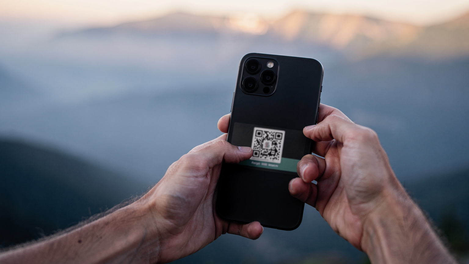 Nærbilde av en hånd som holder en smarttelefon og aktiverer en eSIM ved å skanne en QR-kode, med en fjern utsikt over en tåkete dal i bakgrunnen.