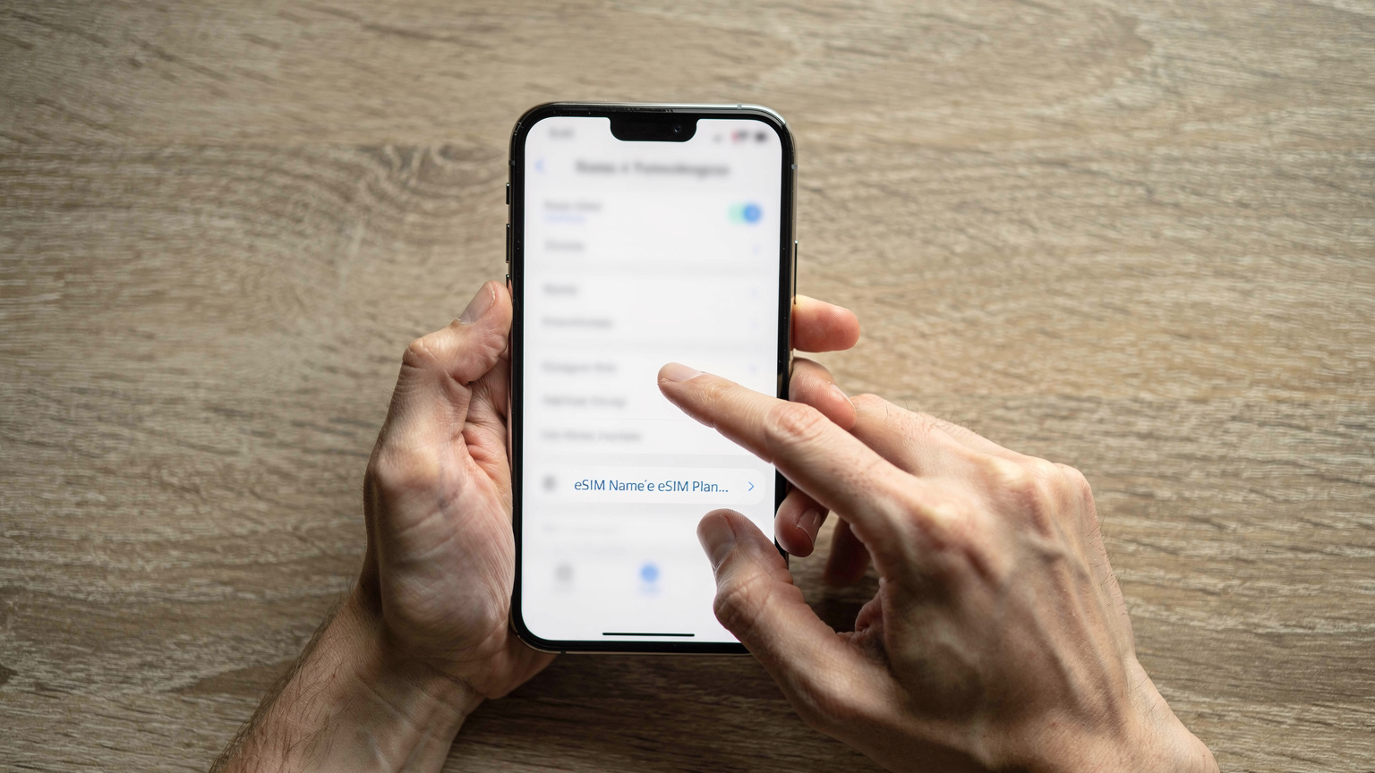 Un primer plano de manos humanas sosteniendo un smartphone, mostrando la pantalla de configuración de una eSIM con la opción de nombrar el plan de datos. No hay texto legible en la pantalla, solo la interfaz de usuario genérica.