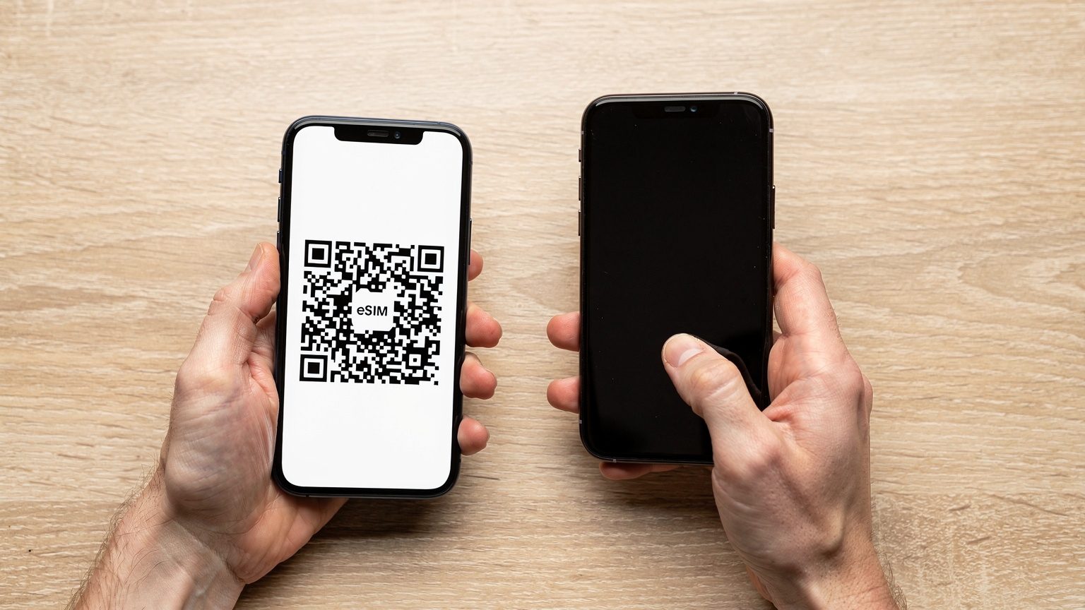 Twee handen die een smartphone vasthouden, waarbij de ene hand het scherm van de telefoon met een QR-code toont en de andere hand een tweede smartphone gebruikt om de QR-code te scannen en de eSIM te installeren.