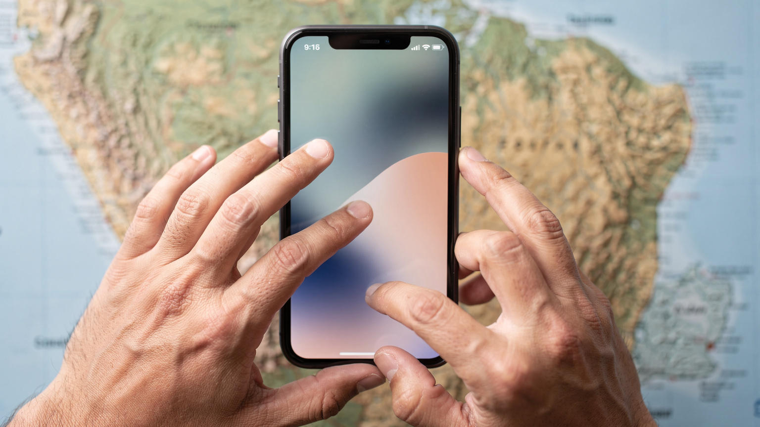 A close-up of a person's hands holding a smartphone, navigating settings or an app, with a blurred map of Ecuador in the background.