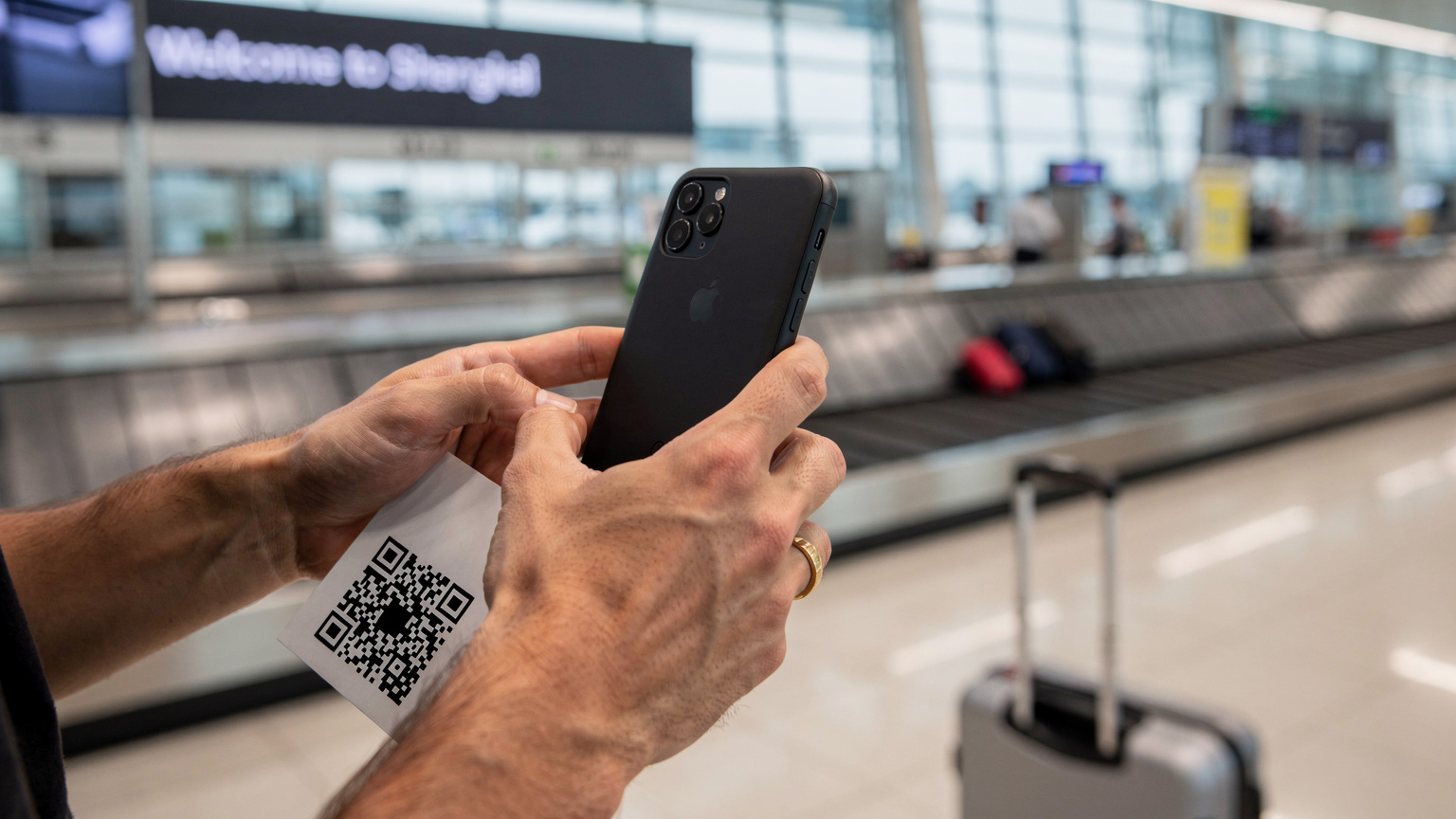 Un viaggiatore sta scansionando un codice QR per attivare la sua eSIM al terminal degli arrivi dell'aeroporto internazionale di Shanghai Pudong, con il suo telefono in primo piano e un bagaglio a mano accanto.