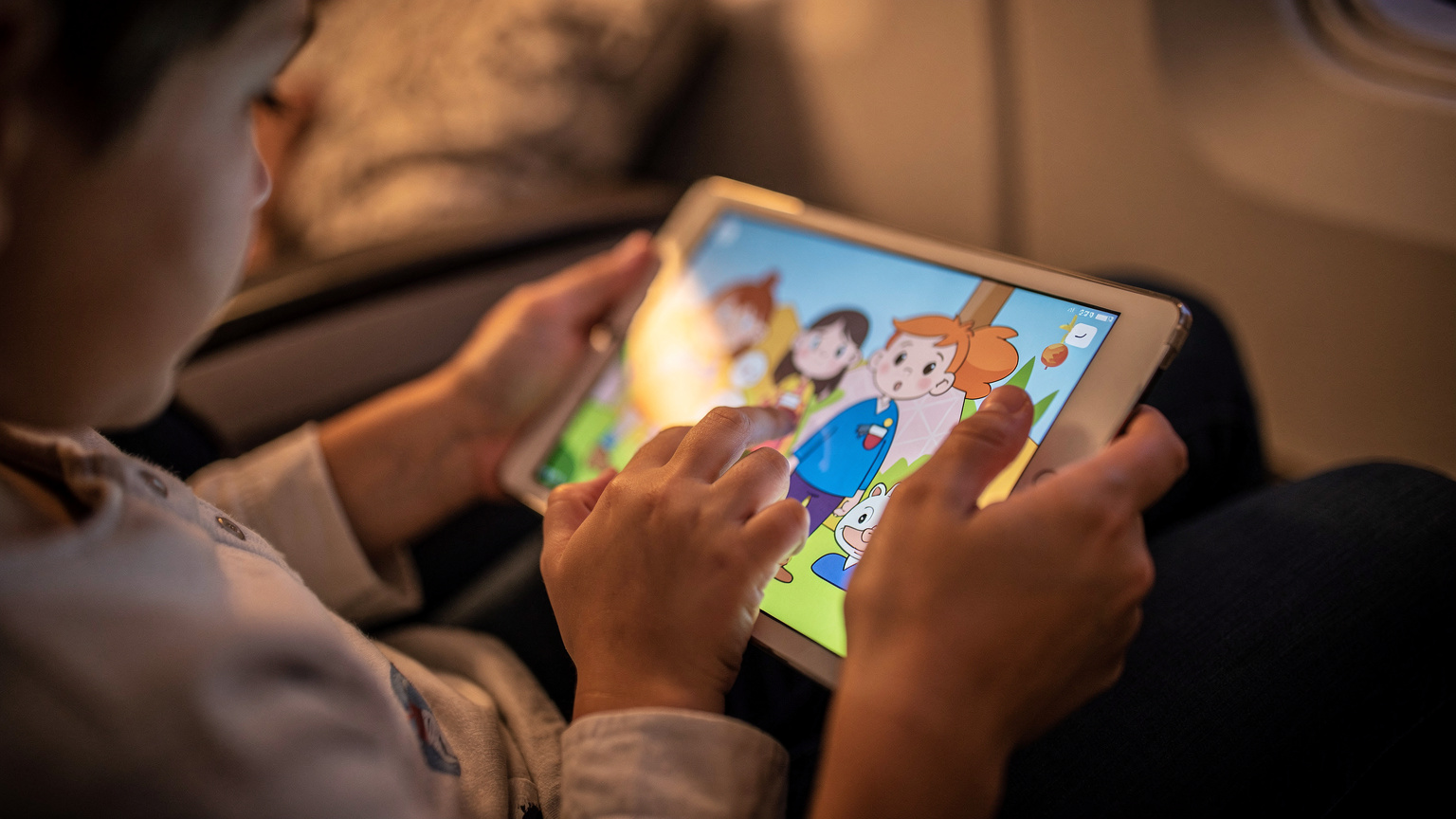 A close-up of a child's hands holding a tablet, displaying a colorful animation, with a parent's hand gently guiding them, perhaps pointing to something on the screen.