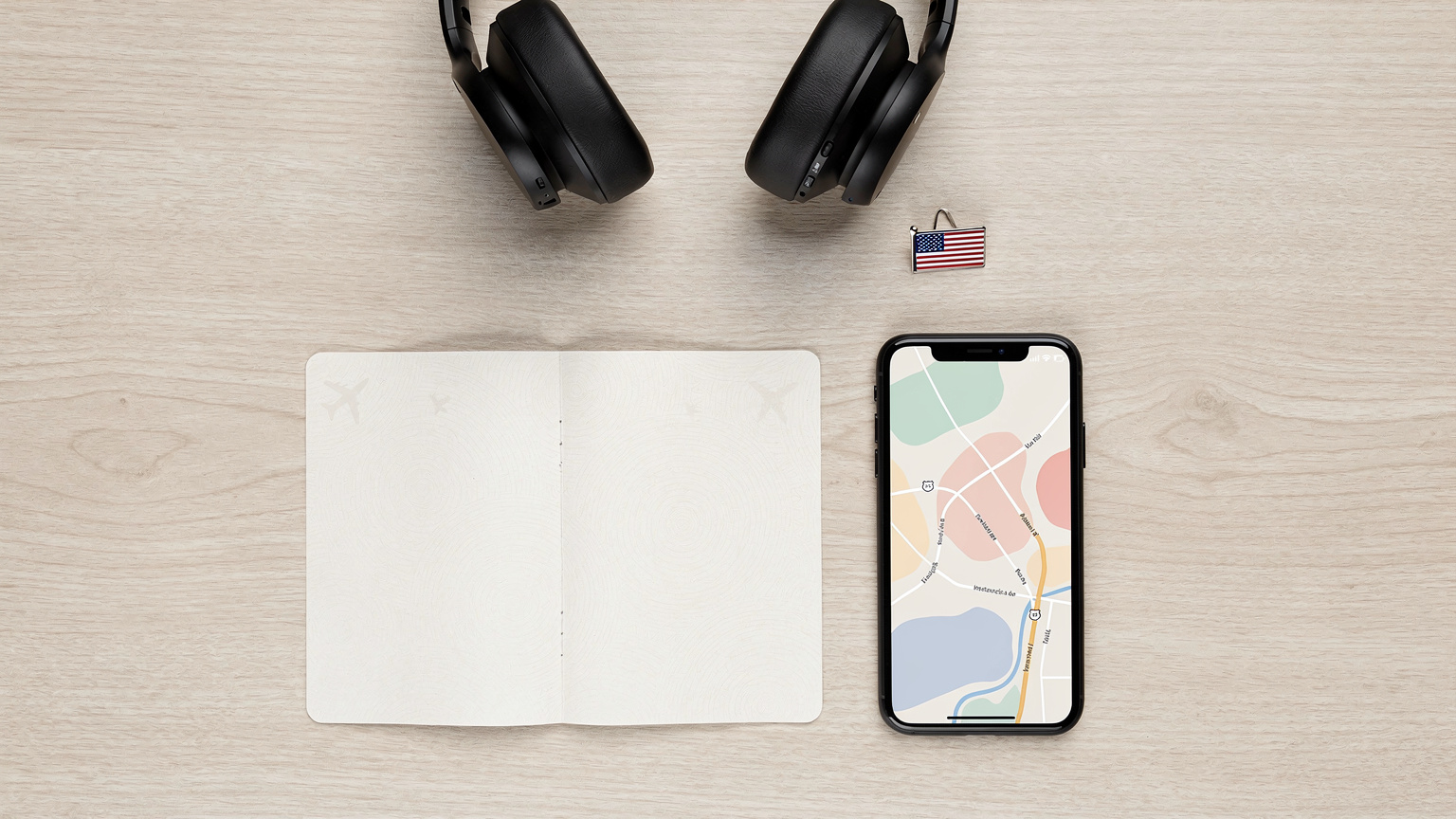 An overhead flat-lay arrangement showcasing a US passport, a smartphone displaying a navigation app, wireless headphones, and a small American flag pin, neatly organized on a wooden desk for travel.
