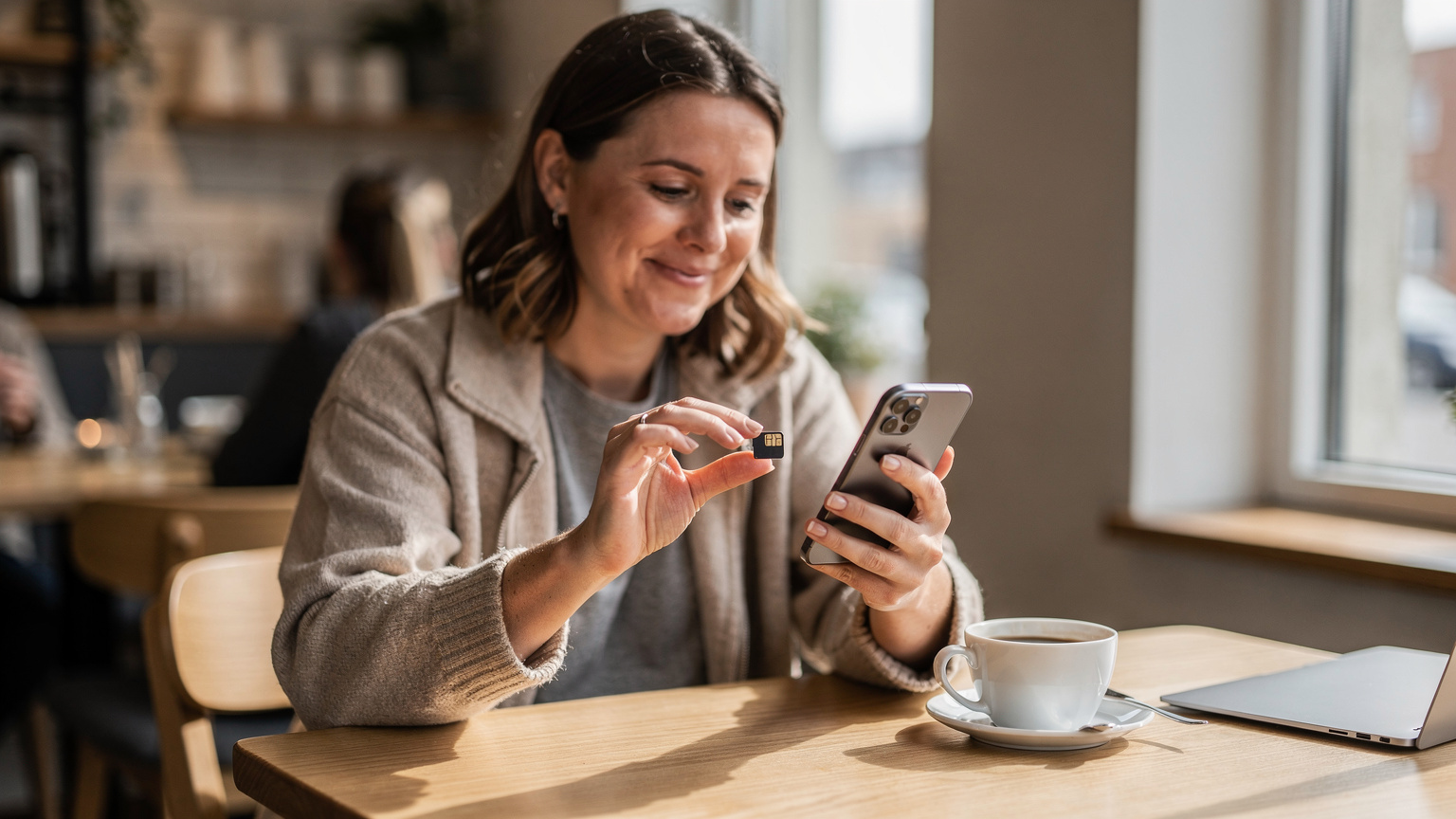 En kvinde holder sin smartphone og et eSIM-kort for at vise det lille, indbyggede format, mens hun sidder på en cafe i Aarhus.