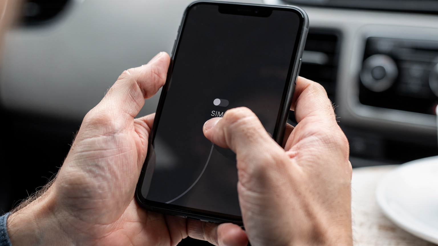 A close-up shot of human hands holding a modern smartphone, with one thumb gently tapping an icon on the screen to switch between cellular data plans, illustrating the ease of eSIM management.