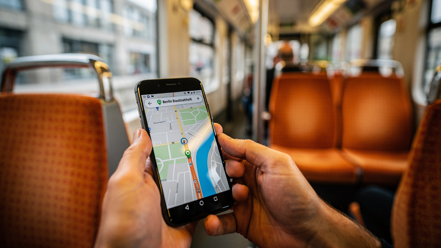 Ein Reisender hält sein Smartphone mit einer geöffneten Karten-App in der Hand, die den Berliner Hauptbahnhof zeigt, während er in einer U-Bahn sitzt.