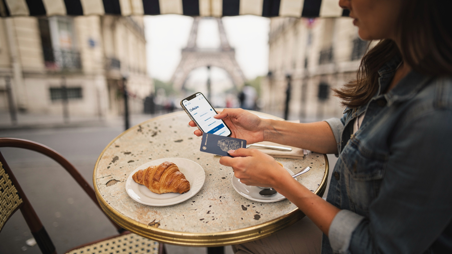 Una donna con un passaporto e un telefono in mano, con la Torre Eiffel sullo sfondo, sta selezionando un piano dati eSIM sull'app Cellesim, mostrando un'interfaccia pulita.