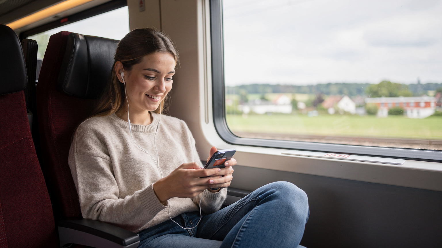 En kvinna tittar på sin telefon ombord på ett tåg, med ett glatt uttryck, efter att framgångsrikt ha aktiverat sitt eSIM.