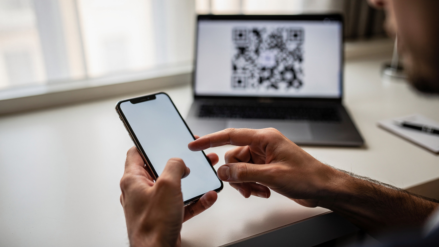 Manos de un profesional remoto interactuando con la pantalla de su teléfono para activar una eSIM, con un código QR visible en otra pantalla.