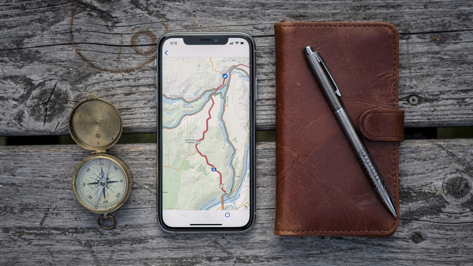 Ein Smartphone zeigt eine Offline-Karte für einen Roadtrip in Kanada, daneben liegen ein Kompass und ein Reisetagebuch, alles auf einem rustikalen Holztisch.
