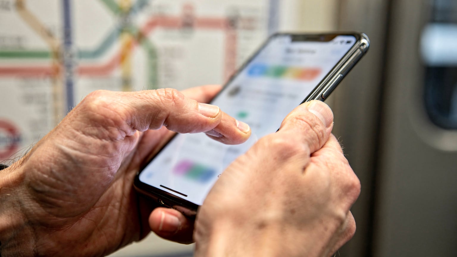 Primer plano de unas manos sosteniendo un smartphone, con el pulgar interactuando con la pantalla para navegar por una aplicación de eSIM, mientras se ve un fondo desenfocado de un mapa de metro de una ciudad europea.