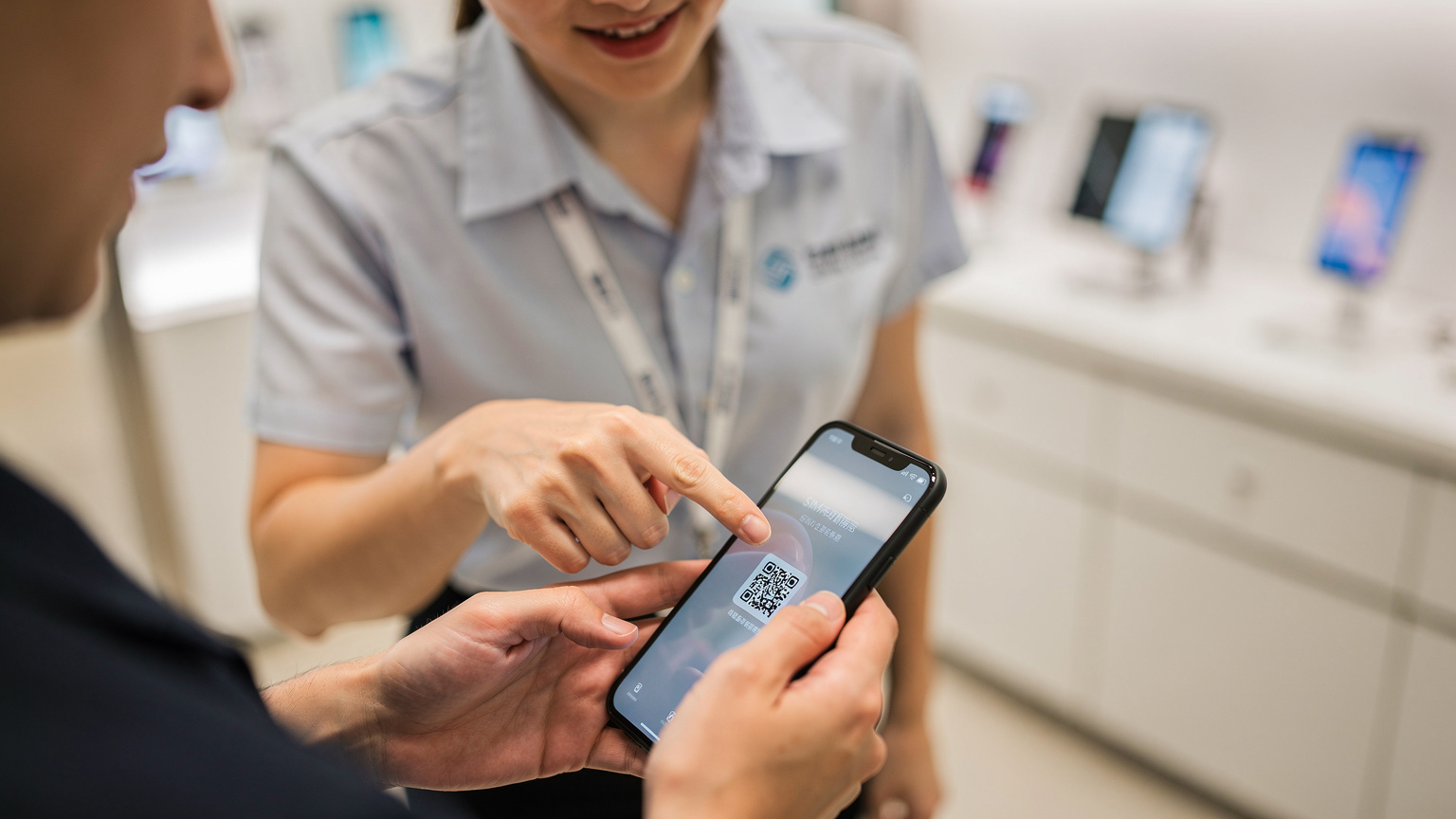 一名中國移動香港的店員正在協助顧客使用手機掃描QR碼激活eSIM,展示了便捷的線下服務體驗。