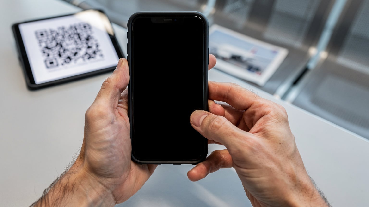 空港の出発ゲートで、搭乗を待つ間にスマートフォンでeSIMの設定を行う旅行者の手元。画面にはQRコードのスキャン画面が表示されている。