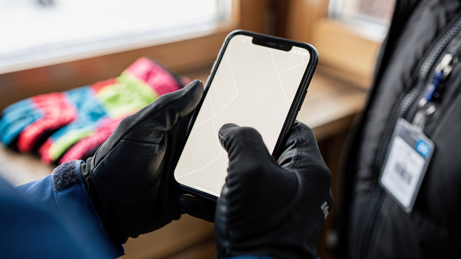 O persoană ține un smartphone în mână, deschizând aplicația de hărți, cu o pereche de mănuși de schi și un bilet de teleschi pe fundal, sugerând planificarea pe pârtie.