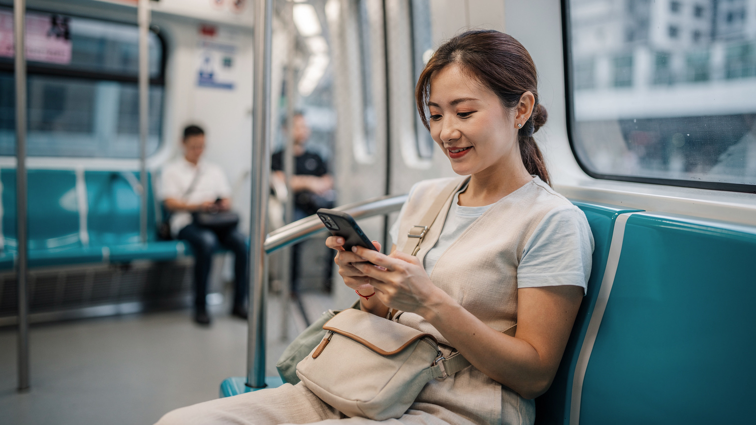 一位中国女性旅客坐在香港港铁的座位上, 她的手机屏幕亮着, 显示正在管理eSIM设置, 脸上带着轻松的微笑。
