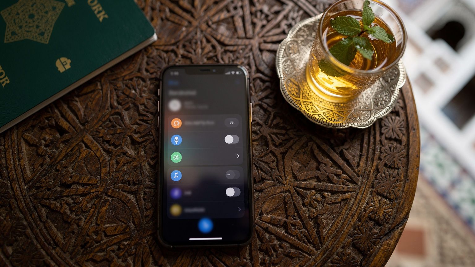 Un téléphone affichant un écran de réglages réseau avec des options de roaming, posé sur une table en bois avec un passeport et une tasse de thé à la menthe traditionnelle marocaine en arrière-plan, dans un riad typique de la médina de Fès.