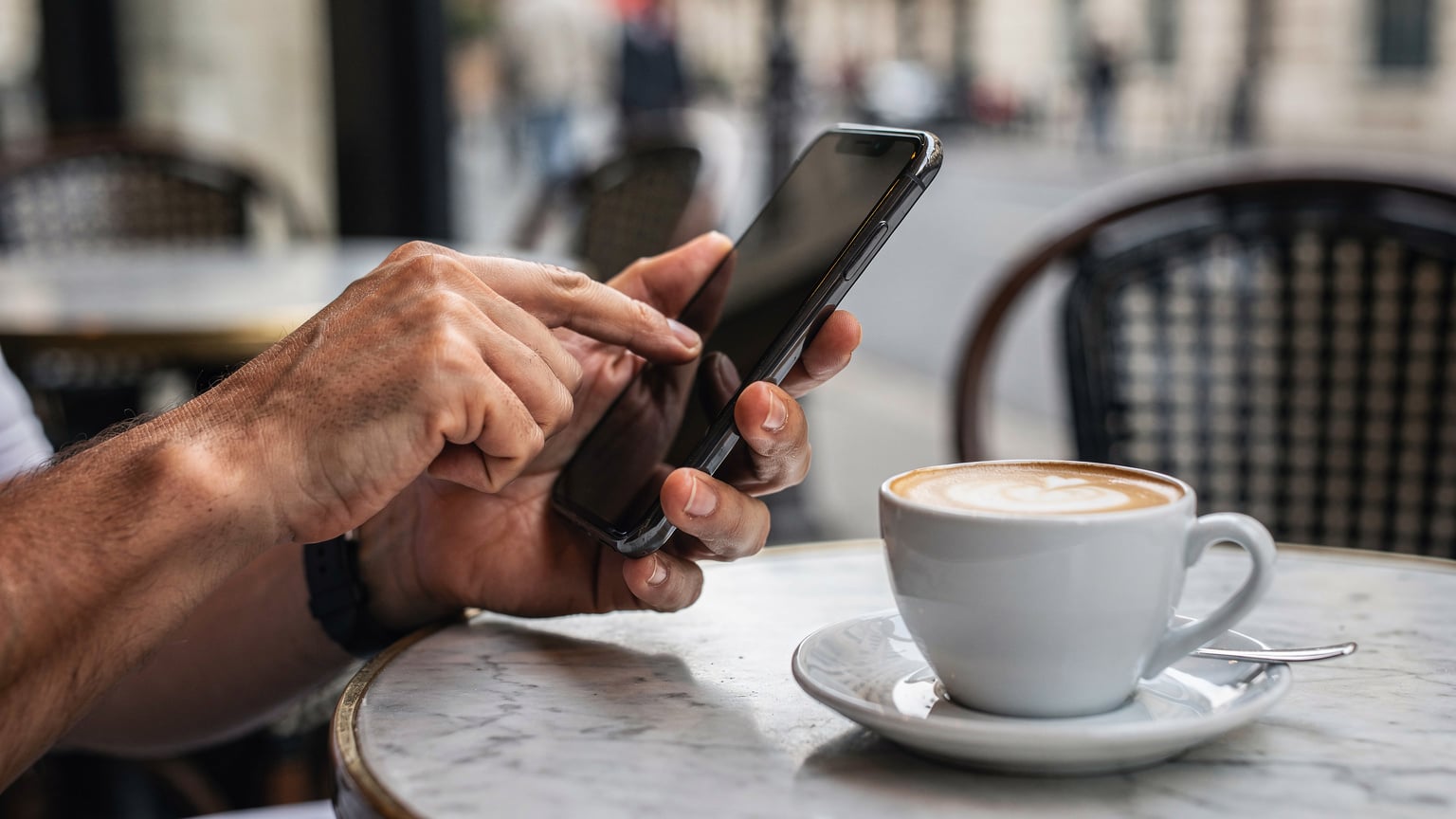 Paris'in bir sokak kafesinde kahve içerken telefonunda eSIM uygulamasını kurma adımlarını gösteren bir seyahatseverin elleri.