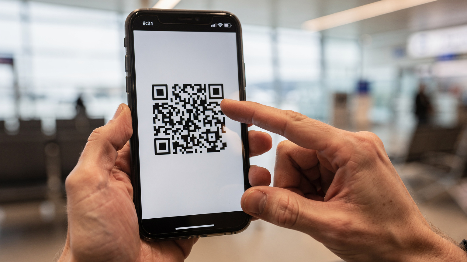 Крупный план рук, держащих смартфон, на экране которого отображается QR-код для активации eSIM, на фоне размытого интерьера аэропорта Пулково.