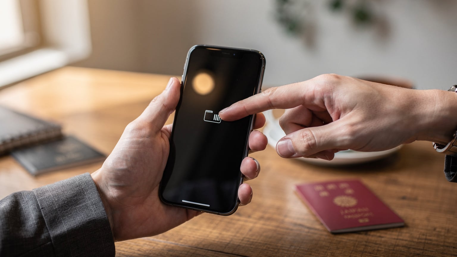 カフェで休憩中、パスポートとコーヒーが置かれたテーブルで、スマートフォンを操作しeSIMの設定を確認する旅行者の手元。