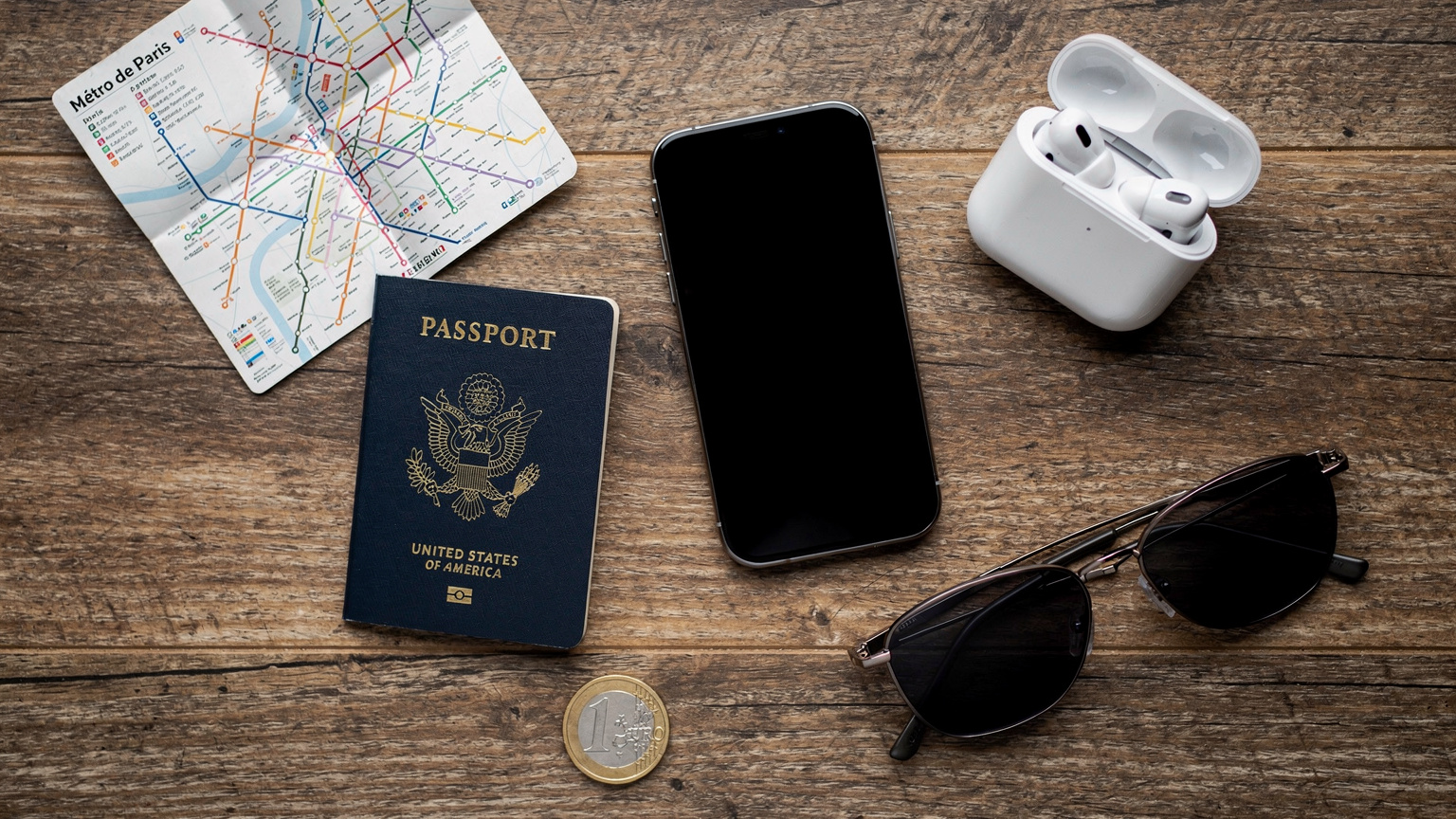 An overhead flat-lay of travel essentials, including a passport, smartphone, headphones, and a local transit map, suggesting readiness for an international trip.