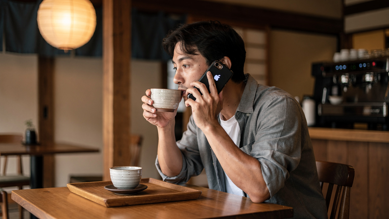 A person sitting at a small table in a cozy Japanese cafe, sipping coffee and using their smartphone to make a call over Wi-Fi.
