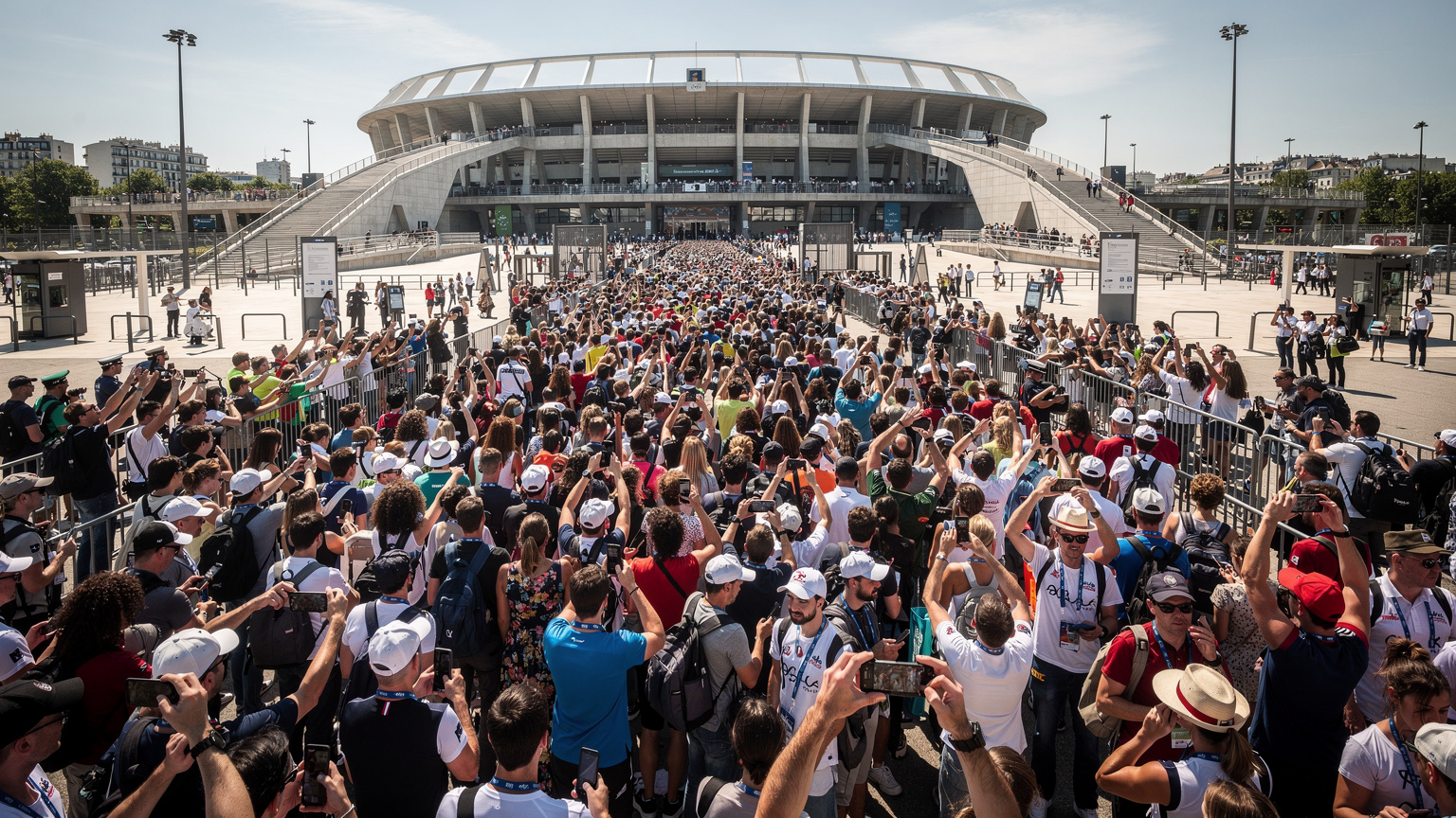 Une foule dense d'athlètes et de spectateurs se presse aux abords d'un site olympique parisien, illustrant la potentielle saturation des réseaux mobiles.