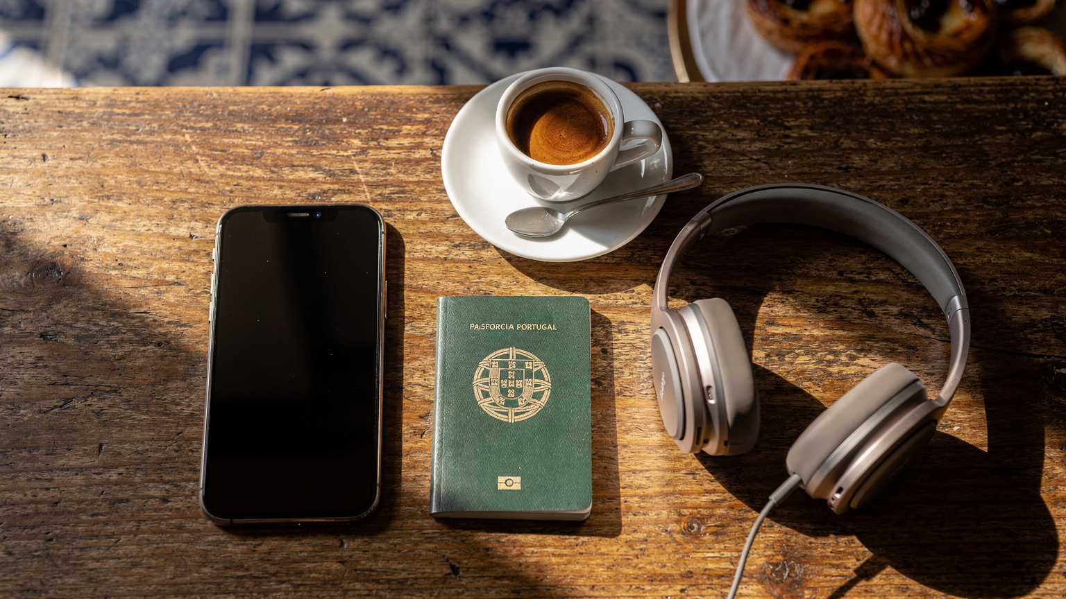Uma mesa de café em Lisboa com um iPhone 18 ao lado de um passaporte e uma xícara de café, simbolizando a facilidade de conectividade para viajantes.