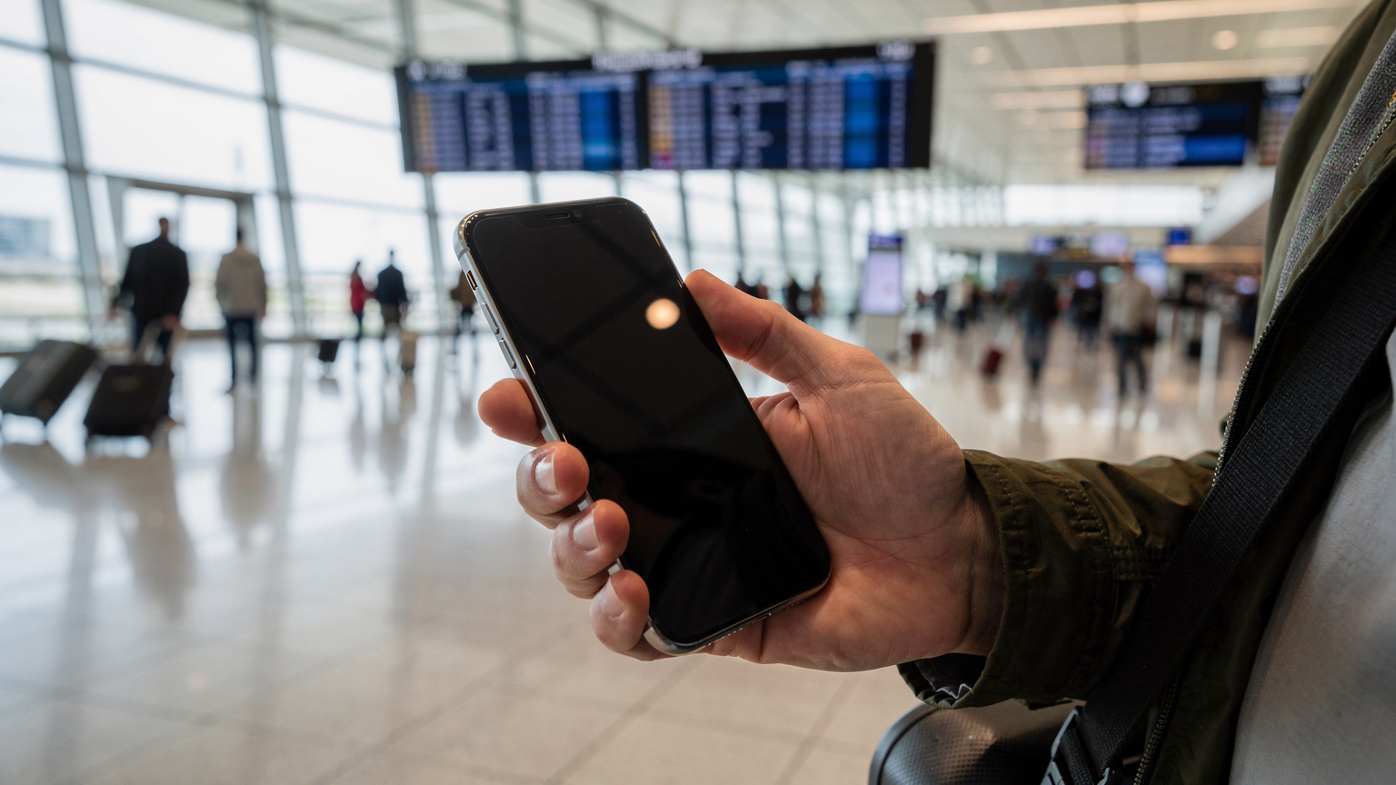 Ein modernes US-iPhone ohne physischen SIM-Slot in der Hand eines Reisenden, der durch ein geschäftiges Flughafenterminal in den USA geht.