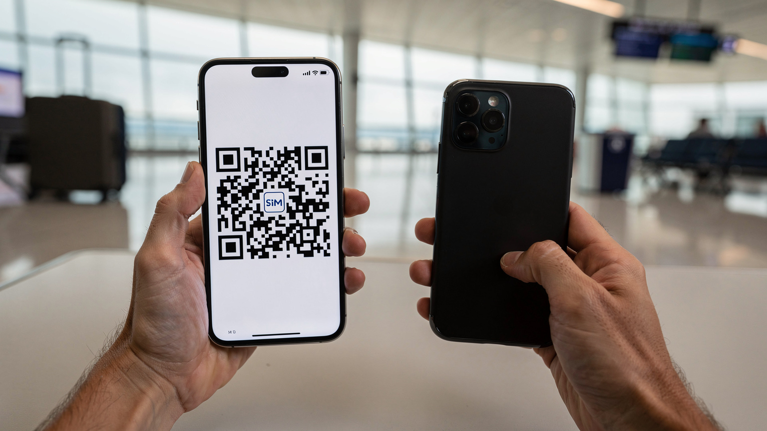 Mani di un viaggiatore che tiene uno smartphone e scannerizza un codice QR per attivare un'eSIM, con uno sfondo sfocato di un terminal aeroportuale.