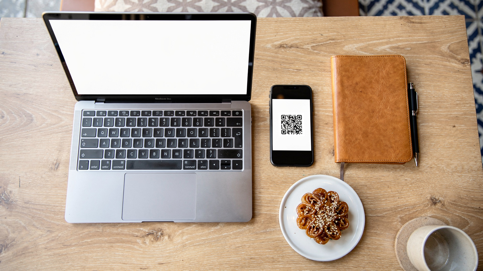 An editorial overhead flat-lay of a digital nomad's workspace in a stylish cafe in Rabat, Morocco, featuring a laptop, a smartphone displaying a QR code for eSIM setup, a travel journal, and a traditional Moroccan pastry.