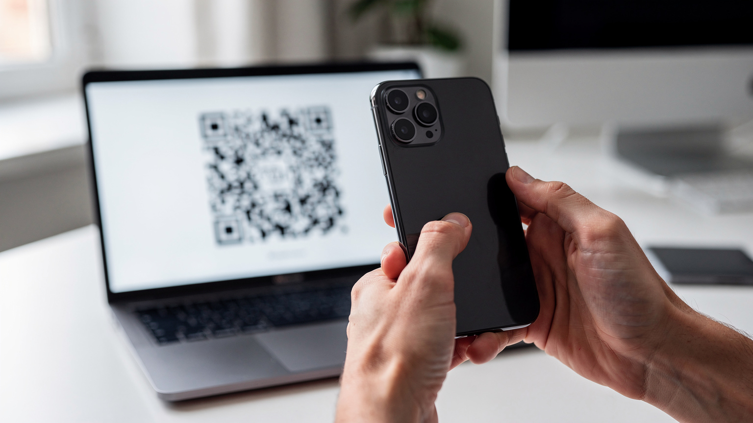 Close-up van handen die zorgvuldig een QR-code scannen vanaf een computerscherm met een nieuwe iPhone, de focus ligt op de interactie tussen apparaat en digitale code.