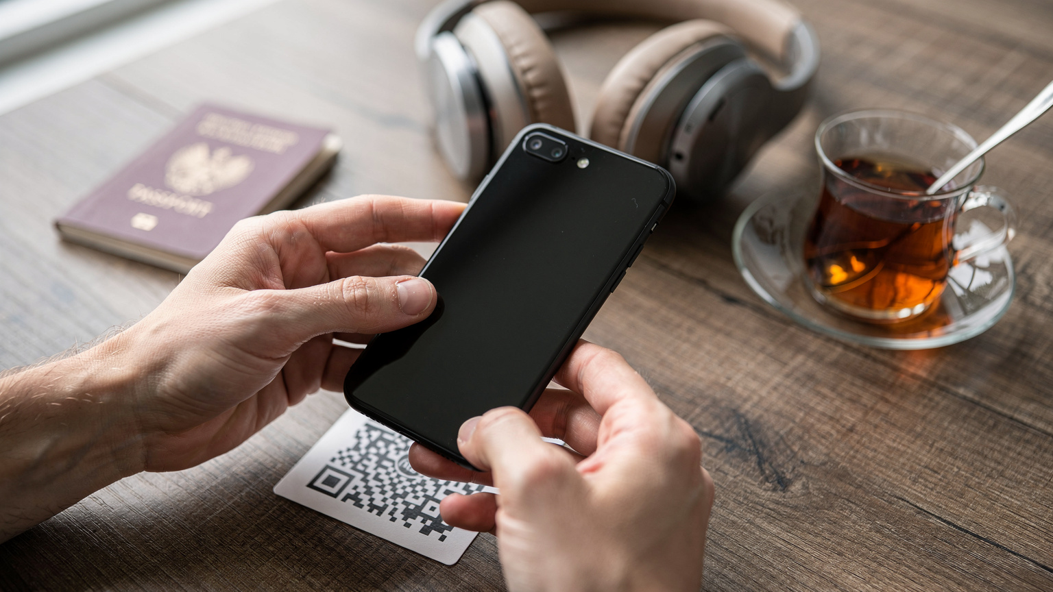 Nahaufnahme von Händen, die ein Smartphone halten, auf dem ein QR-Code für die eSIM-Installation gescannt wird, im Hintergrund ein Reisepass und eine Tasse türkischer Tee.
