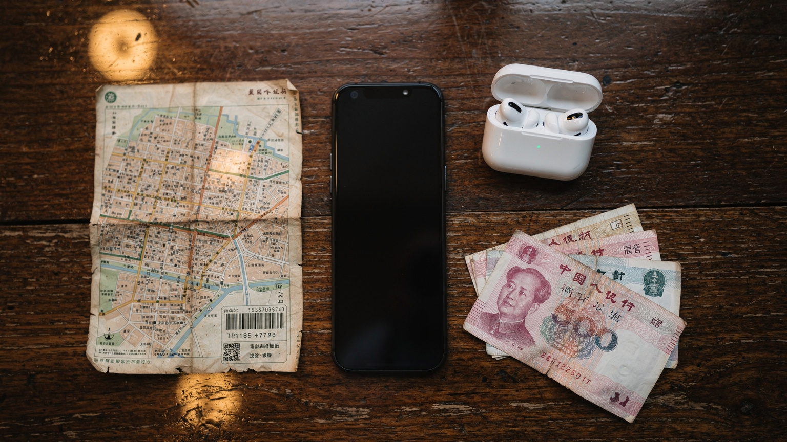 一張俯視圖，展示了一張地圖、一部智能手機、護照、耳機和當地貨幣（人民幣）等旅行必需品，整齊地擺放在一張咖啡館的木桌上，營造出準備出發的氛圍。