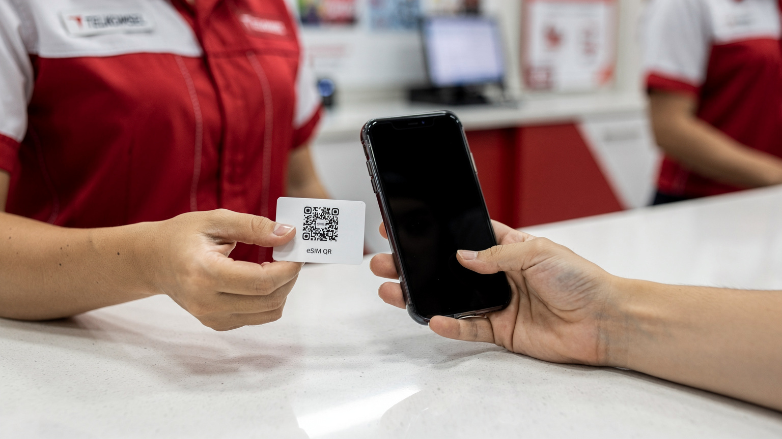 Tangan seorang petugas GraPARI menyerahkan QR code eSIM kepada pelanggan yang sedang memegang ponsel, mengilustrasikan proses migrasi eSIM secara langsung di konter layanan.