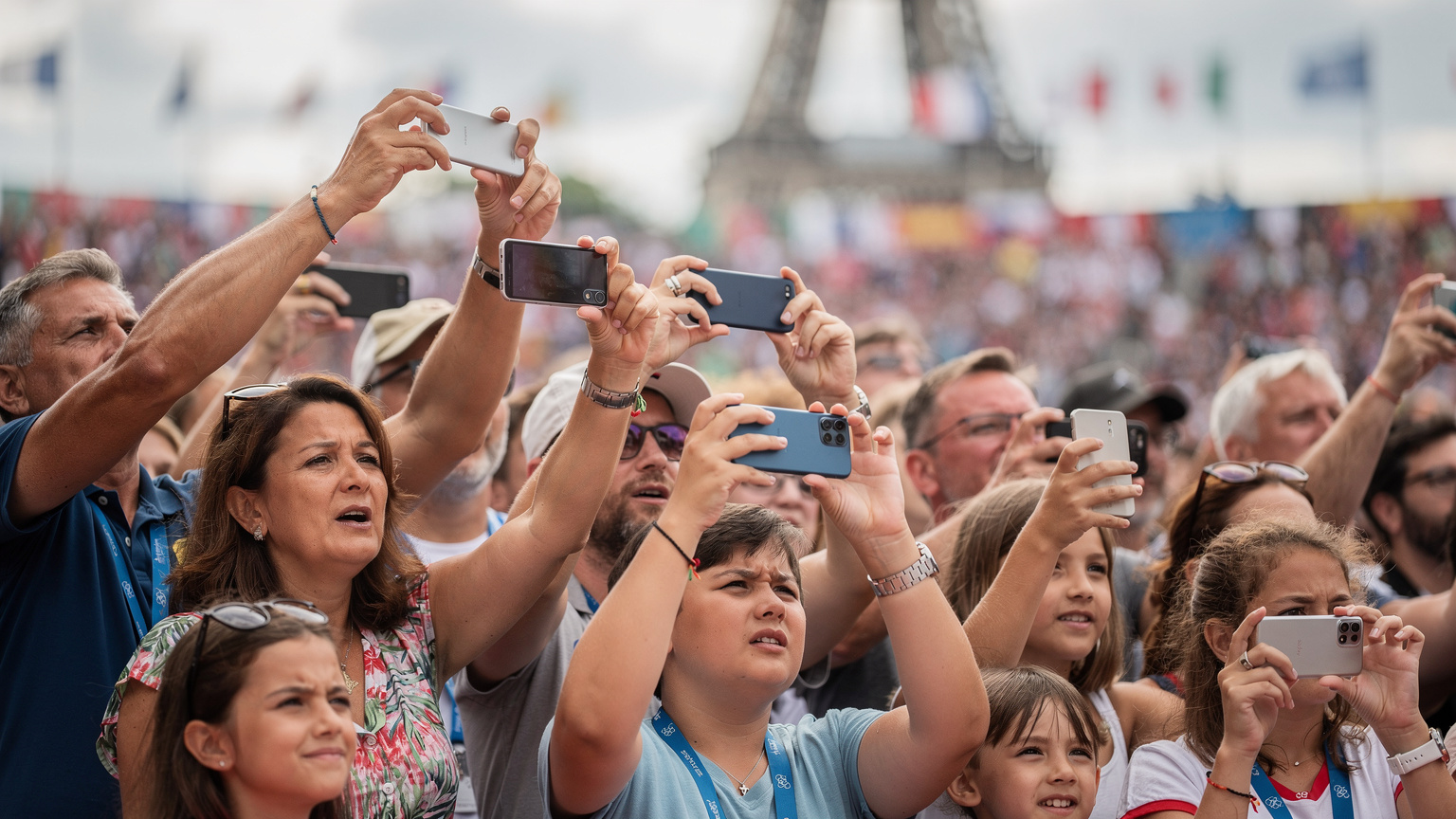 Un groupe de spectateurs enthousiastes, dont des parents et des enfants, utilise leurs smartphones pour photographier ou filmer un événement sportif en plein air à Paris, avec une atmosphère de joie et d'excitation palpable.