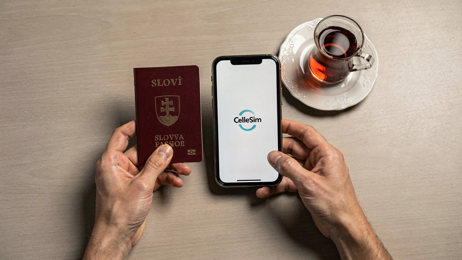 Detailný záber na ruky cestovateľa, ktorý drží pas a smartfón s logom Cellesim na displeji, ležiace na stole letiskového salónika vedľa šálky tureckého čaju.