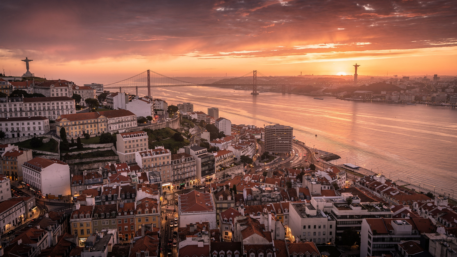 Uma vista aérea da paisagem urbana de Lisboa ao pôr do sol, com o rio Tejo brilhando, simbolizando a modernidade e a beleza da capital portuguesa.