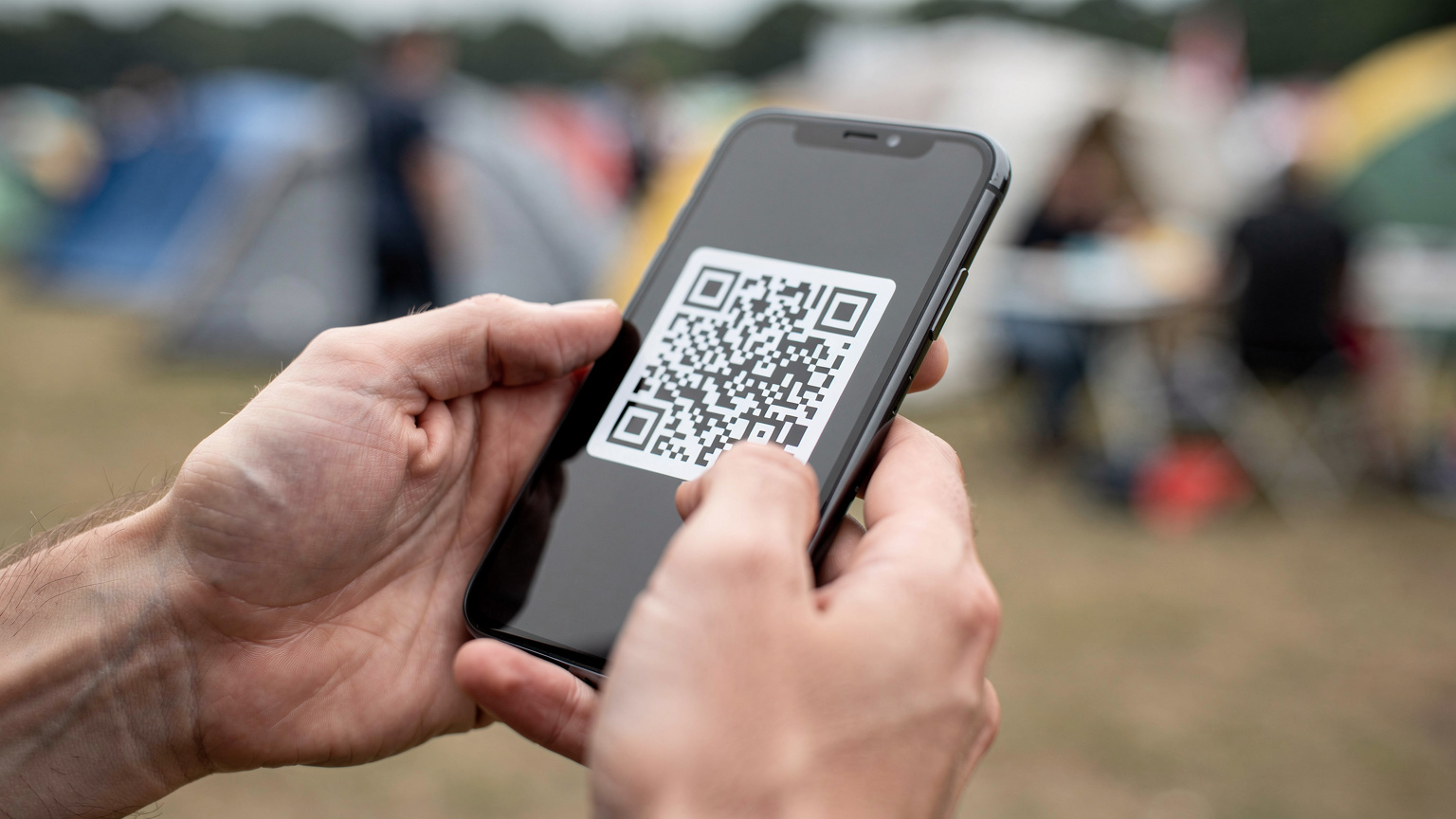 Крупний план рук людини, яка тримає смартфон і сканує QR-код для активації eSIM. На фоні видно розмиті обриси натовпу фестивалю та наметів, підкреслюючи легкість та швидкість процесу активації.
