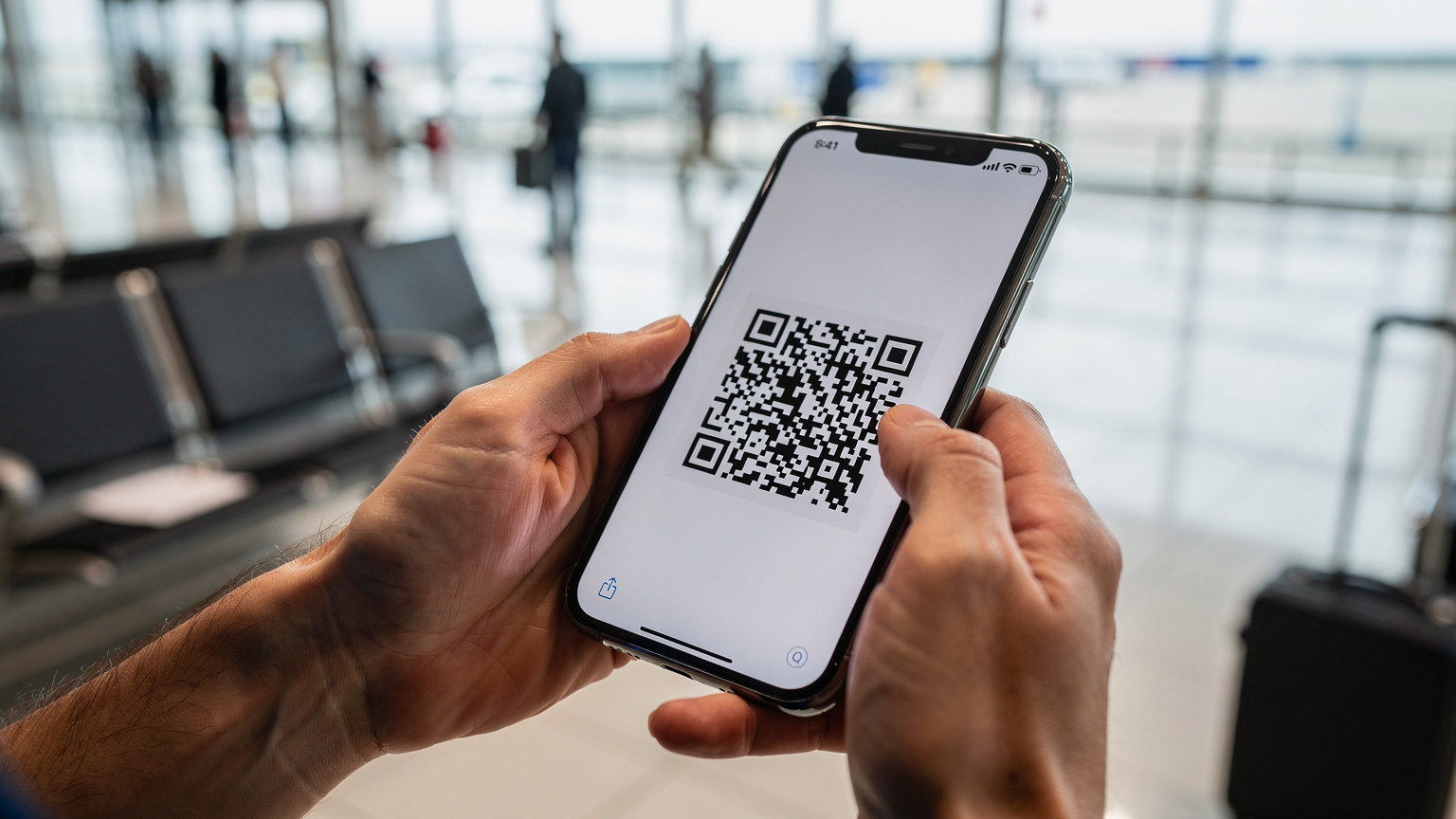 Närbild på händer som håller en smartphone och skannar en QR-kod för eSIM-aktivering, med en suddig bakgrund av en modern flygplatsterminal.