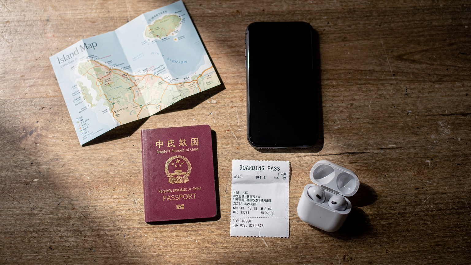 一个俯拍的旅行者桌面，桌上散落着一本护照、一张登机牌、一部智能手机（屏幕熄灭）、一副无线耳机和一张当地的旅游地图。物品摆放随意但有序，光线柔和。