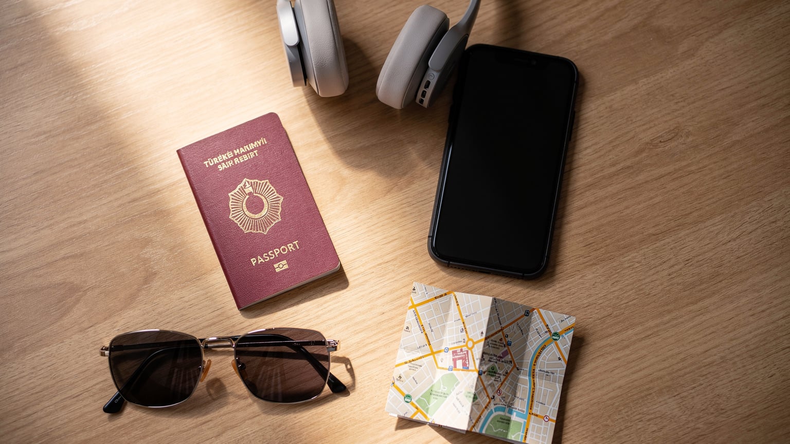 Bir masanın üzerinde pasaport, akıllı telefon, kulaklık ve harita parçası gibi seyahat aksesuarları düzenli bir şekilde duruyor.