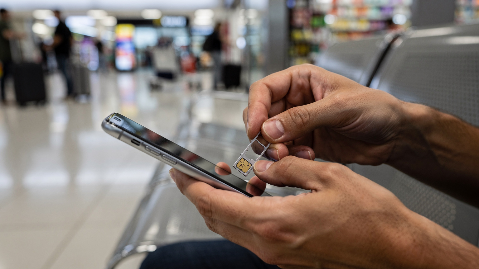 Una persona frustrada intenta configurar una SIM física en un concurrido aeropuerto latinoamericano.