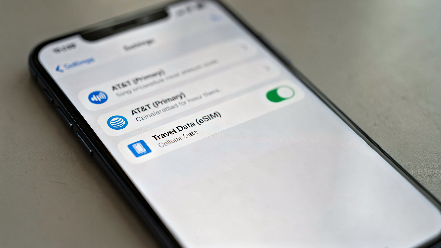 A close-up shot of a smartphone screen showing dual-SIM settings, with one line labeled 'AT&T (Primary)' and another 'Travel Data (eSIM)', highlighting the data preference selection.
