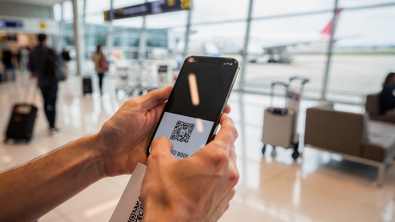 Ένας ταξιδιώτης σκανάρει έναν QR κωδικό eSIM στο κινητό του, ενώ βρίσκεται σε ένα σύγχρονο αεροδρόμιο στην Ευρώπη, με βαλίτσες και άλλους ταξιδιώτες στο φόντο.