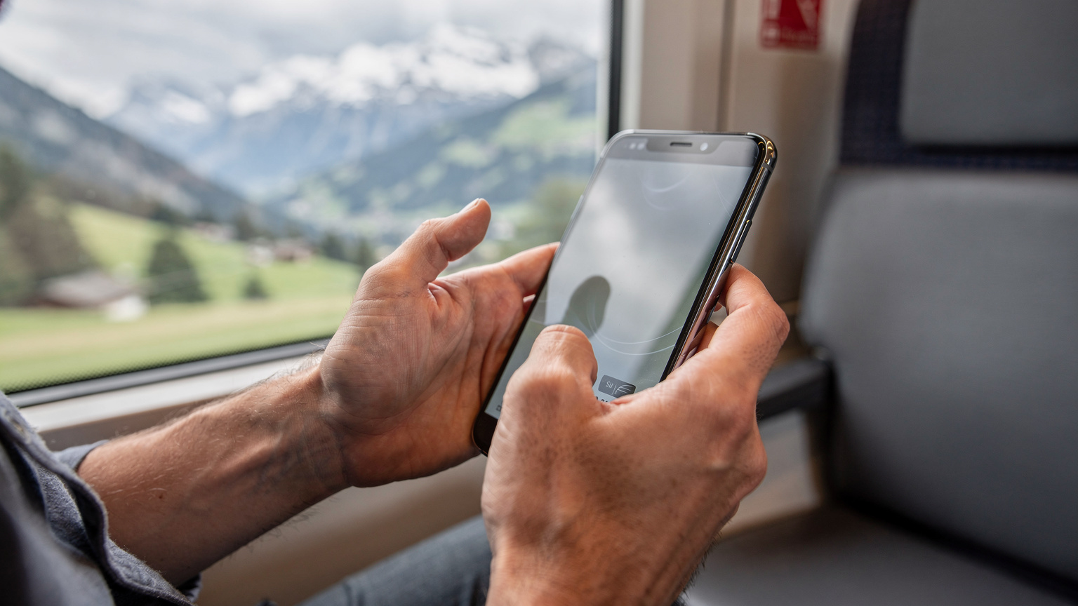 Manos de un viajero escaneando un código QR para activar una eSIM en su teléfono dentro de un tren SBB, con un paisaje montañoso pasando por la ventana.