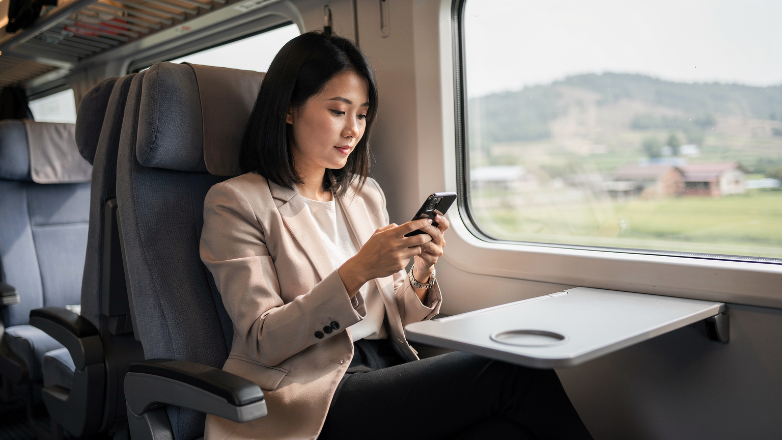Seorang wanita muda Asia yang bergaya, sibuk memeriksa telefon pintarnya di dalam gerabak kereta api laju China yang moden, dengan pemandangan luar bandar yang samar-samar di luar tingkap.